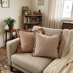 a cozy room with a beige sofa that has two pillows and a blanket. Both pillows are 100% cotton and have ruffles. One pillow is gingham and the other is brown. Pillows are 20x20 in size and have a zipper to remove the insert. 