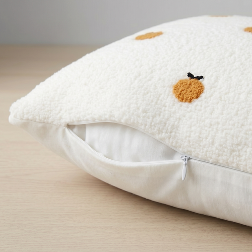 White pillow with embroidered orange design on a beige surface. Showcasing pillow's zipper for easy removal.