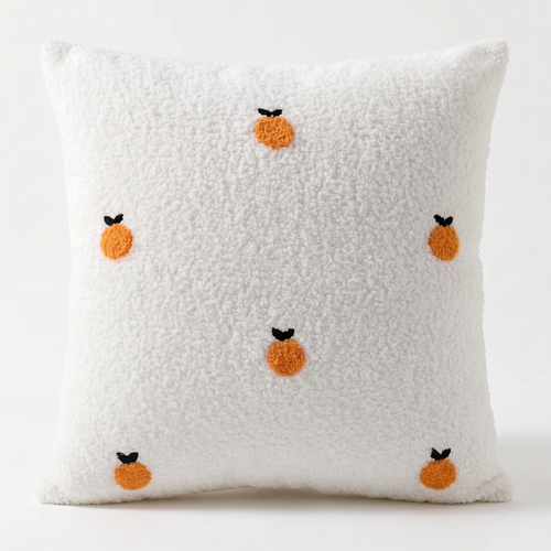 White pillow with orange fruit embroidered design on a white background