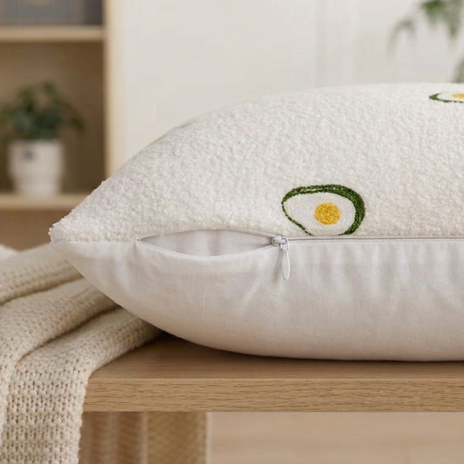 White pillow with embroidered avocado design on a wooden surface