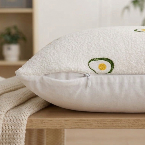 White pillow with embroidered avocado design on a wooden surface