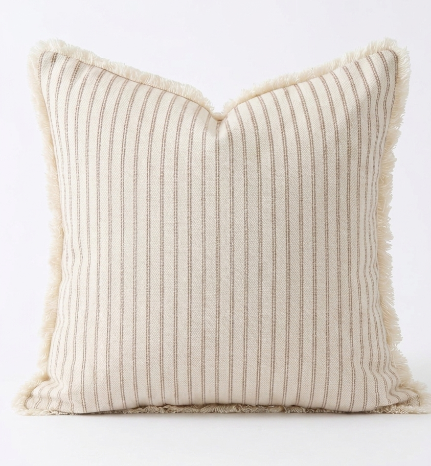 A square throw pillow with vertical beige stripes on a cream background and fringed edges, photographed against a plain white background. Great for Beach style decor. Pillow cover has a zipper so cover can be removed and washed. Insert sold separately. 