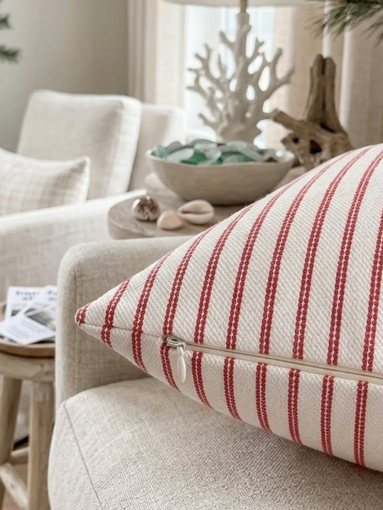 A close-up of a square throw pillow with red and white vertical stripes and it's highlighting the zipper on the throw pillow. It is removable and washable. Insert sold separately. Setting is a beach inspired interior. 