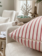 A close-up of a square throw pillow with red and white vertical stripes and it's highlighting the zipper on the throw pillow. It is removable and washable. Insert sold separately. Setting is a beach inspired interior. 