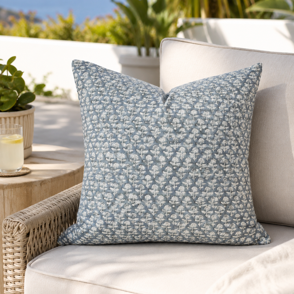 Blue patterned pillow on a white outdoor sofa with plants and a table in the background