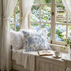 Cozy window seat with floral throw pillows, surrounded by white curtains and hydrangeas outside.