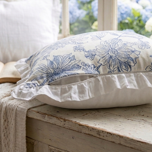 Blue and white floral-patterned pillow on a wooden surface with hydrangeas in the background
