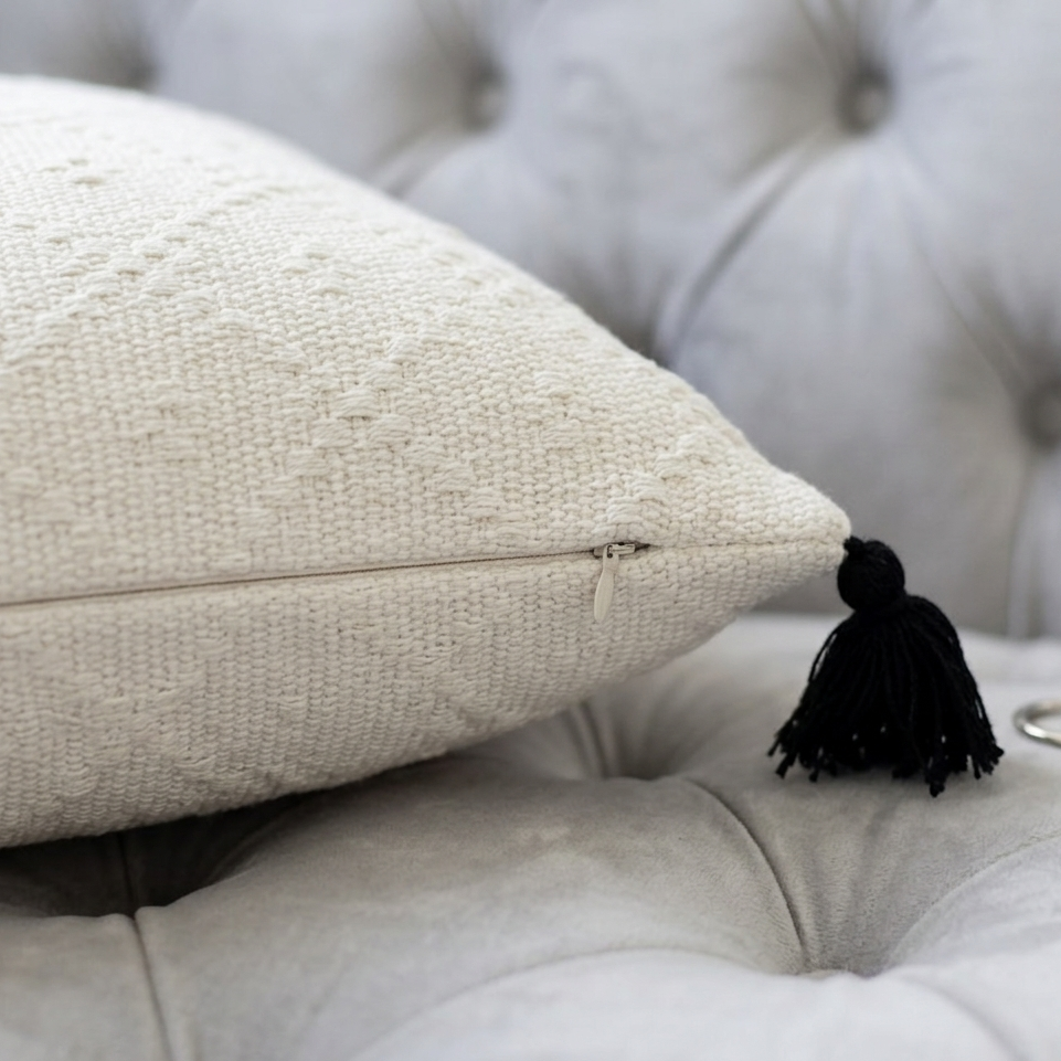 Textured white pillow cover with a black tassel on a gray tufted sofa.