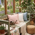 Decorative bench with colorful, scalloped edge pillows and a floral blanket in a garden setting