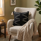 Cozy living room with a beige armchair, black pillow with white patterns, and a knitted blanket.